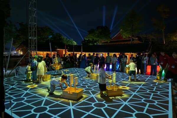 Hour of Decision at Unjudang — children play the interactive floor game under searchlights, Tongjeyoung: Light of Peace